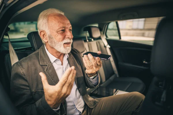 朝の通勤中に車の後部座席に座っている間に彼のスマートフォン上で音声メッセージを作る成功したシニアビジネスマンのショット — ストック写真