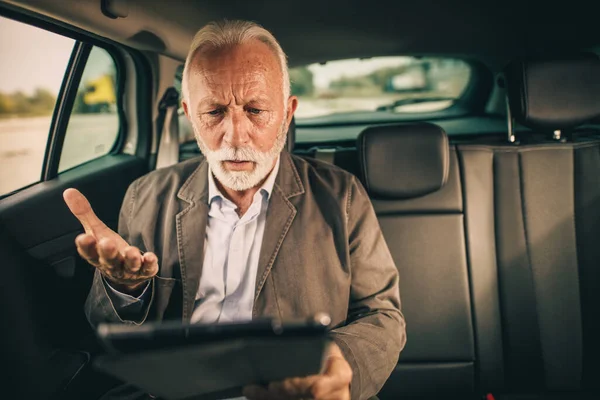 彼の朝の通勤中に車の後部座席に座っている間 デジタルタブレットを使用して心配している上級ビジネスマンのショット — ストック写真