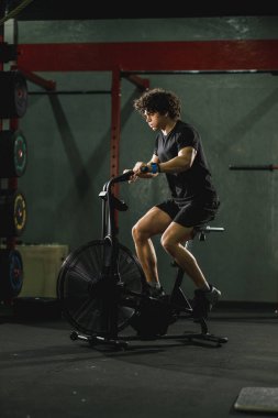 Kaslı bir adam spor salonunda bisiklet egzersizi yapıyor..