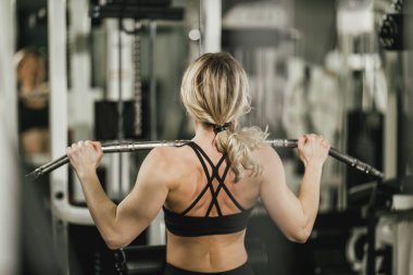 Genç, kaslı bir kadın spor salonunda makineyle antrenman yapıyor..