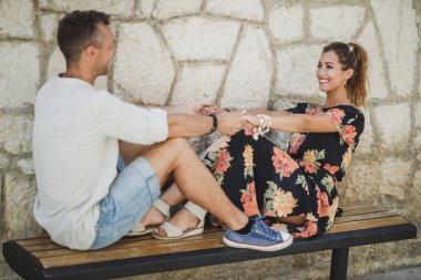 Mutlu çift, eski Akdeniz şehrinde yaz gününü geçirirken bankta oturup eğleniyor..