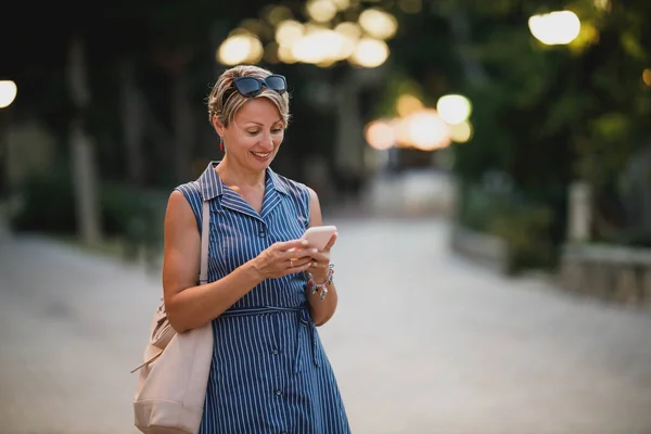 Mujer Atractiva Madura Usando Teléfono Inteligente Caminando Por Noche Mientras —  Fotos de Stock