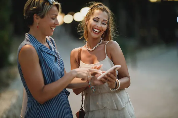 Duas Jovens Mulheres Atraentes Estão Divertindo Usando Celular Juntos Enquanto — Fotografia de Stock