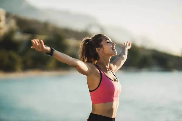 年轻健康的女人在靠近海面运动后张开双臂呼吸和放松 — 图库照片