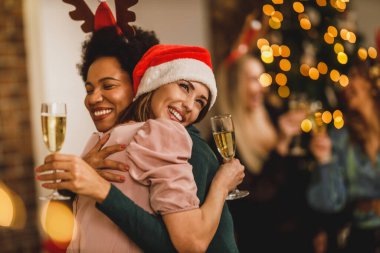 Çok ırklı bayan arkadaşlar Noel 'i ya da yeni yılı kutlamak için evde toplandılar. Şampanya ile kadeh kaldırıyorum..