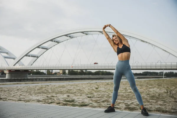Smiling Sporty Young Woman Warm Stretching Her Arms While Exercising — стоковое фото