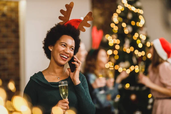 お祝いの雰囲気の中で新年のパーティーでスマートフォンで話す幸せなアフリカ系アメリカ人女性 — ストック写真