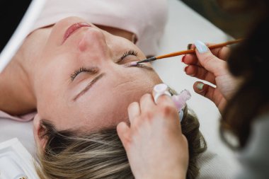 Tanınmayan bir güzellik uzmanı güzellik salonundaki kaş kaplama prosedürünün bir parçası olarak keratin sürmüş bir modelin kaşlarını kaplıyor..
