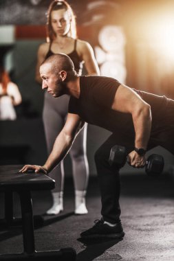 Beden eğitimi hocası spor salonunda formda genç bir bayana sırt kası egzersizi yapıyor..