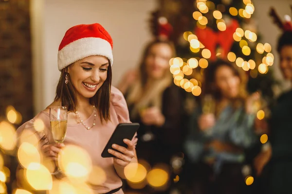お祝いの雰囲気の中で新年のホームパーティーでスマートフォンにメッセージを送信幸せな若い女性 — ストック写真