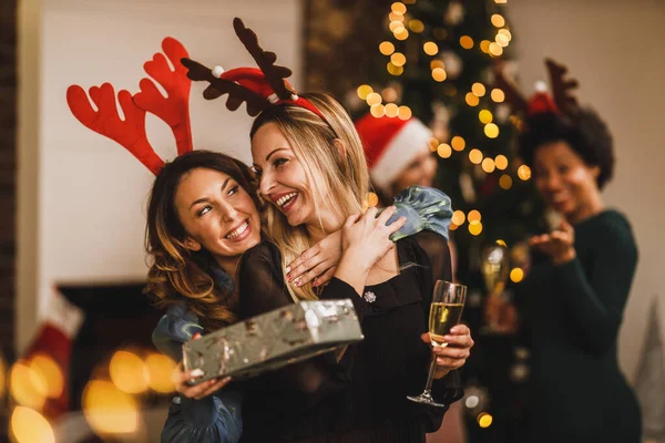 クリスマスや新年を祝うために家に集まりながら 抱き合ってプレゼントを渡す女性の友人を笑顔 — ストック写真