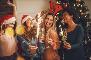 Dört neşeli çoklu etnik kız Noel 'de ya da yeni yıl partisinde şampanya içerken maytaplarla eğleniyor..