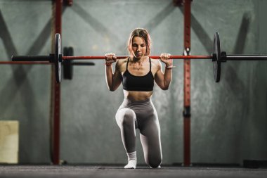Spor salonundaki sıkı çalışmada formda genç bir bayan. Halterle hamle egzersizi yapıyor..