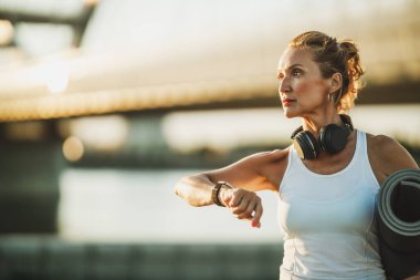 Şehirdeki nehir kenarındaki eğitimden sonra yoga minderiyle gezen orta yaşlı, zinde bir kadın..