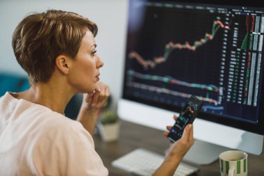 Merkez büroda bilgisayar ve akıllı telefon üzerinde çalışırken orta yaşlı kadın kripto para ticareti yapıyor..