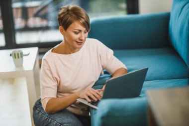 Salgın karantina sırasında evindeki ofisinde dizüstü bilgisayarla çalışan orta yaşlı bir kadın serbest yazar..