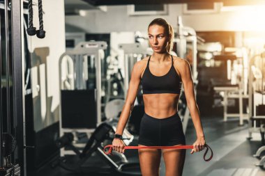 Genç, kaslı bir kadın, direniş bandıyla egzersiz yaparken spor salonunda sıkı bir antrenman için hazırlanıyor..