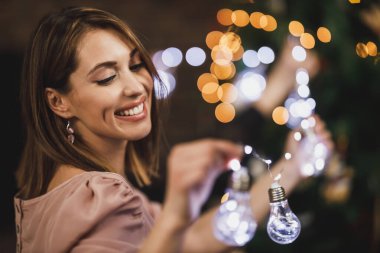 Güzel genç bir kadın evini Noel lambalarıyla süslüyor ve tatilin tadını çıkarıyor..