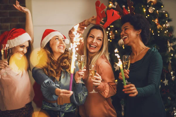 4人の陽気な多民族の女の子が一緒にクリスマスや新年のパーティーでシャンパンを楽しみながら輝きを楽しんでいます — ストック写真