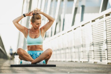 Orta yaşlı bir kadın saçını bağlıyor ve nehir köprüsünde eğitime hazırlanıyor..