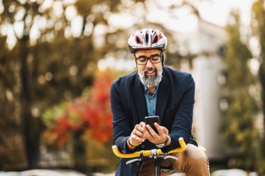 Başarılı bir orta yaşlı işadamı işe bisikletle giderken akıllı telefon kullanıyor..