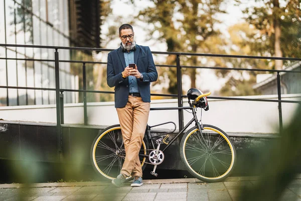 自転車の隣に立つ中高年実業家で 市内で働くために旅行中にスマートフォンを使用しています — ストック写真