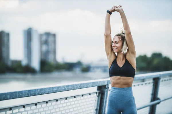 在城里的桥上锻炼身体的时候 年轻的 面带微笑的女人正在热身 张开双臂 — 图库照片