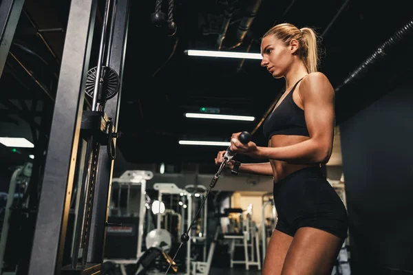 若い筋肉質の女性はジムで機械の訓練をしている 彼女は重い体重で彼女の両足の筋肉を汲み上げている — ストック写真