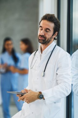 Hastane koridorunda hızlı bir mola verirken dijital tablet kullanan yorgun bir doktor..