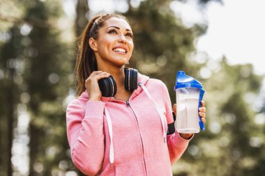 Genç, güzel, gülümseyen bayan koşucu doğada koştuktan sonra mola veriyor..