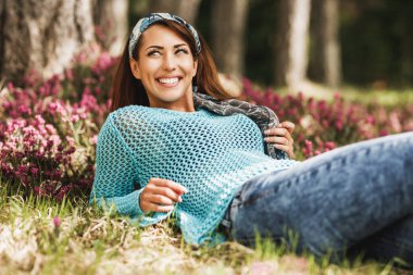 Çiçekli çimenlerde uzanan ve güneşli bahar gününün tadını çıkaran güzel, genç bir kadın..