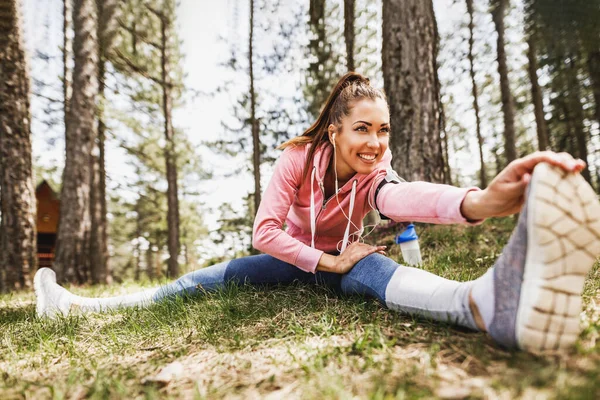 Young Beautiful Smiling Female Runner Listening Music While Stretching Jogging — стоковое фото