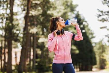 Genç, güzel, gülümseyen bayan koşucu doğada koşuya hazırlanıyor..