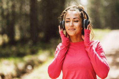 Genç, güzel, gülümseyen bayan koşucu müzik dinliyor ve dışarıda koşuya hazırlanıyor..