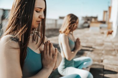 Two young women practicing yoga on a rooftop terrace.