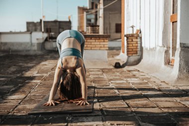 Rahat genç bir kadın terasta yoga yapıyor..