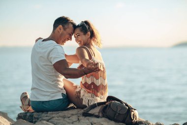 Sevgi dolu, neşeli bir çift, deniz taşında oturup, kumsala yakın bir yaz tatilinin tadını çıkarırken eğleniyor..