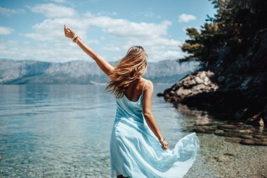 Mavi elbiseli güzel bir kadın güneşli bir günde kumsalda dans edip eğleniyor..