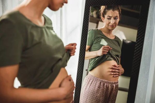 Unhappy Young Woman Standing Front Mirror Holding Hands Her Stomach — Stockfoto