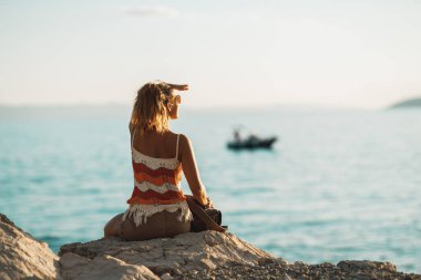 Rear view of an attractive young woman is enjoying a summer vacation while sitting and looking on seaside.