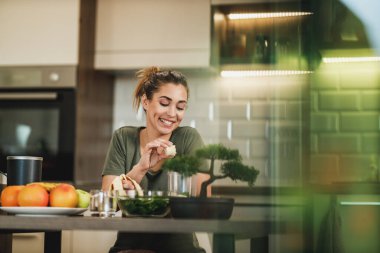 Young woman daydreaming while enjoying morning and preparing a smoothie at home.
