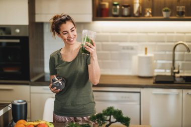 Shot of a young smiling woman making a healthy smoothie in the kitchen at home.