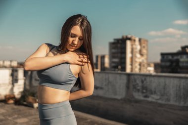 Young pretty woman practicing yoga on a rooftop terrace. City buildings in the background.