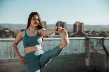 Young woman practicing yoga while doing workout outdoors on a rooftop terrace.