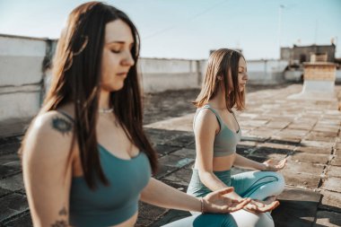 Two young women practicing yoga on a rooftop terrace.