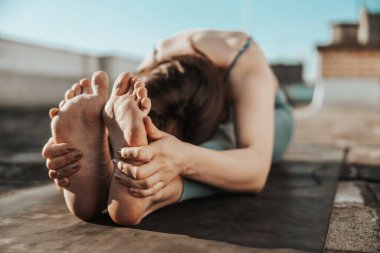 Close-up of a woman practicing yoga stretching exercise on a rooftop terrace.