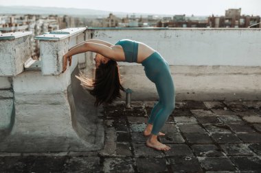 Relaxed woman practicing yoga bridge pose near to wall on a rooftop terrace.