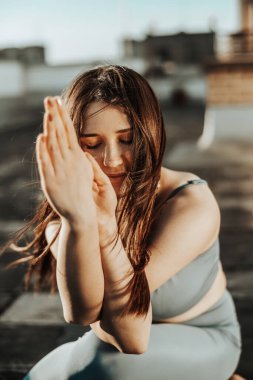 Relaxed woman practicing yoga on a rooftop terrace at sunset.