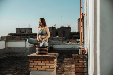Relaxed woman practicing yoga meditating on a rooftop terrace.