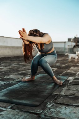 Relaxed woman practicing yoga stretching exercise on a rooftop terrace at sunset.